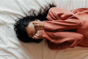 Overhead view of a woman covering her face on bed.