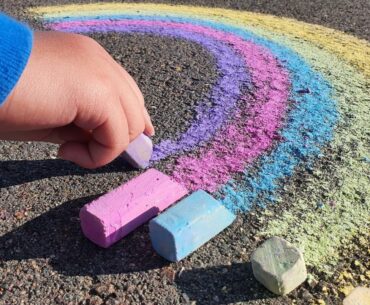 Close up of childs hand drawing a chalk rainbow for LGBTQ Pride.