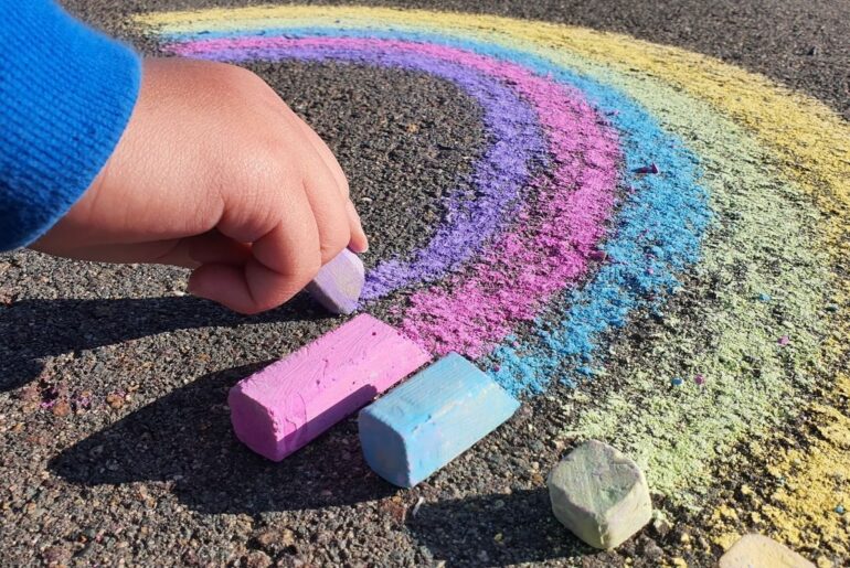 Close up of childs hand drawing a chalk rainbow for LGBTQ Pride.