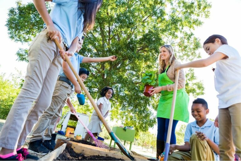 Teacher and students plant vegetables in school garden.