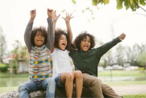 Boys sitting outdoors cheering happily with arms raised overhead.