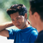 Asian American father and teen son talking.