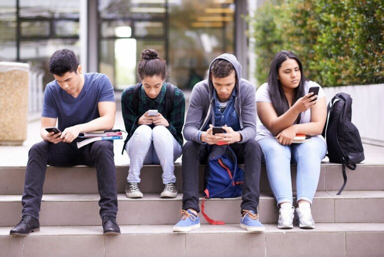 Four teens sitting outside distracted by phones.