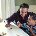 Smiling woman coloring at a table with young boy.