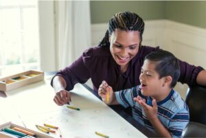 Smiling woman coloring at a table with young boy.