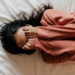 Tween girl shown overhead lying on bed with face covered by her hands.