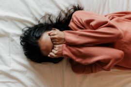 Tween girl shown overhead lying on bed with face covered by her hands.