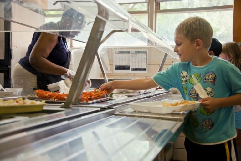 Boy picking up food in school lunch line.