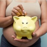 Pregnant woman holding yellow piggy bank.