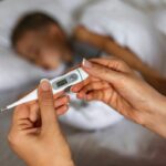 Sick boy in bed with thermometer in foreground.