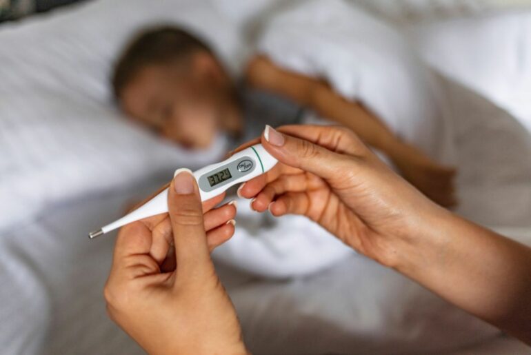 Sick boy in bed with thermometer in foreground.