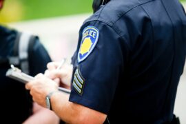 Arm and torso of a police officer issue a ticket to a person wearing a backpack