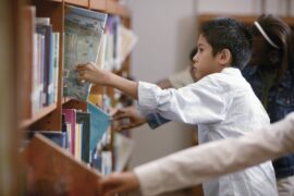 A few children of various races and skin colors selecting picture books from library shelves