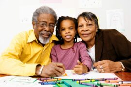 Grandparents and grandchild smiling and coloring together with crayons