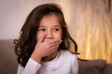 Kid with long dark brown hair covers mouth as if she just said or did something in error