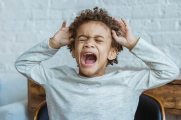 Kid with curly hair and light brown skin screaming and having a meltdown