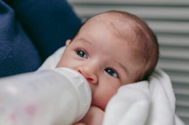 An infant in an adult's arms, drinking from a bottle