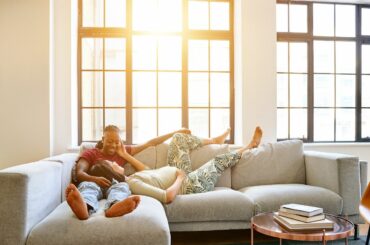 Tired couple relaxing on couch, one looks pregnant and has her head in the other's lap