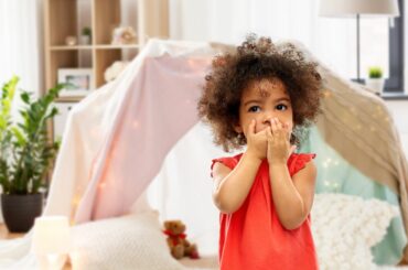 Little kid with curly hair covers her mouth in confusion