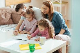 Two white parents and two white children at a table drawing with crayons together