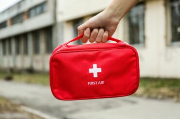 A hand holding a red first aid kit outdoors