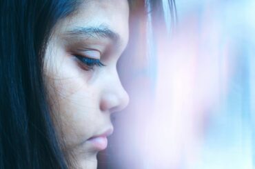 Closeup profile of a teen with long black hair looking down with sad expression