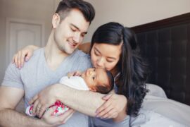 One parent holds a newborn baby while the other parent kisses the baby's forehead