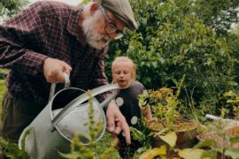 Photo of an older man and a child watering some plants in a garden.