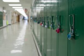An empty school hallway lined with green lockers and fluorescent lighting