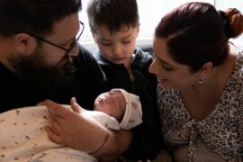 A young boy looks at newborn baby alongside his parents