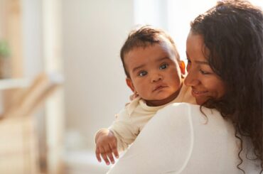 A mom smiles and holds a baby who looks alert as if something has caught its attention