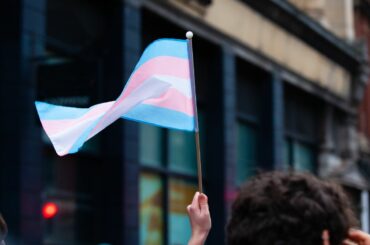 Trans students and their parents ask Education Department leaders to help them fight anti-LGBTQ+ bills A hand holds a trans pride flag outside of a building