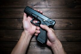 Two hands hold a handgun above a wooden background