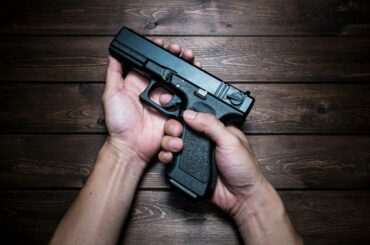 Two hands hold a handgun above a wooden background