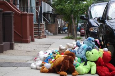 In a large pile of stuffed animals on a city sidewalk, a blue Stitch character on top reads in marker, "R.I.P. Tykeem" for a victim of gun violence.