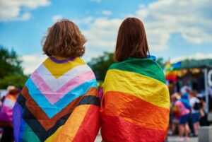 two people with backs turned with Pride flags draped over their shoulders