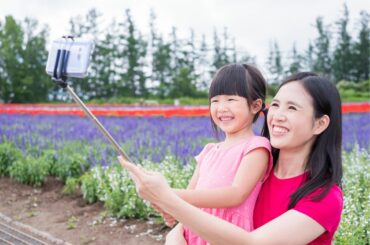 Asian mother and daughter use a selfie stick to take a photo together in front of a field of flowers