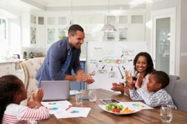 A family of four clapping and smiling at the dining room table, a whiteboard outlining chores in the background
