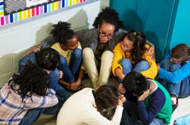 A teach huddles on the floor with elementary students in the corner of a classroom for a safety or lockdown drill