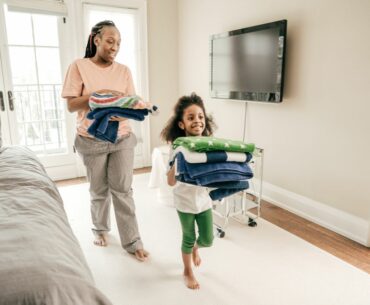 A Black parent and child walk in bare feet and smile while carrying folded towels