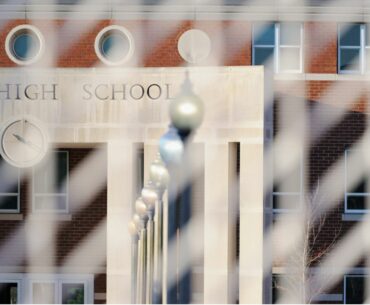 Metal school security fence around a brick and concrete building with an all-caps sign reading "high school"