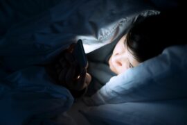 A person under the covers during the dark of the night staring at the glow of a smartphone