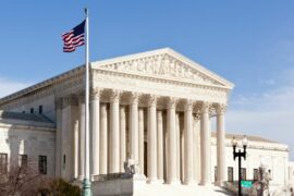 The front of the Supreme Court building with its massive white columns and a U.S. flag flying