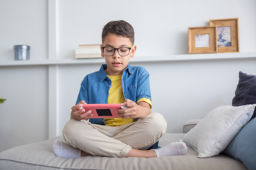 A child plays a game on a device while sitting on a couch