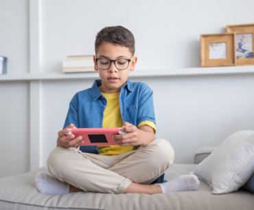 A child plays a game on a device while sitting on a couch