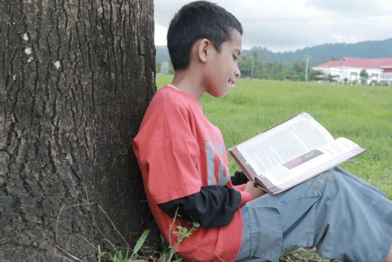 Boy reading book outdoors