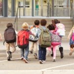 A group of elementary school aged kids arrive at the entrance to school