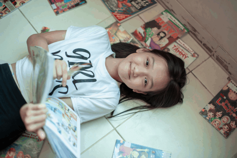 5 graphic novels to help combat the reading crisis Girl lying with comic books and graphic novels
